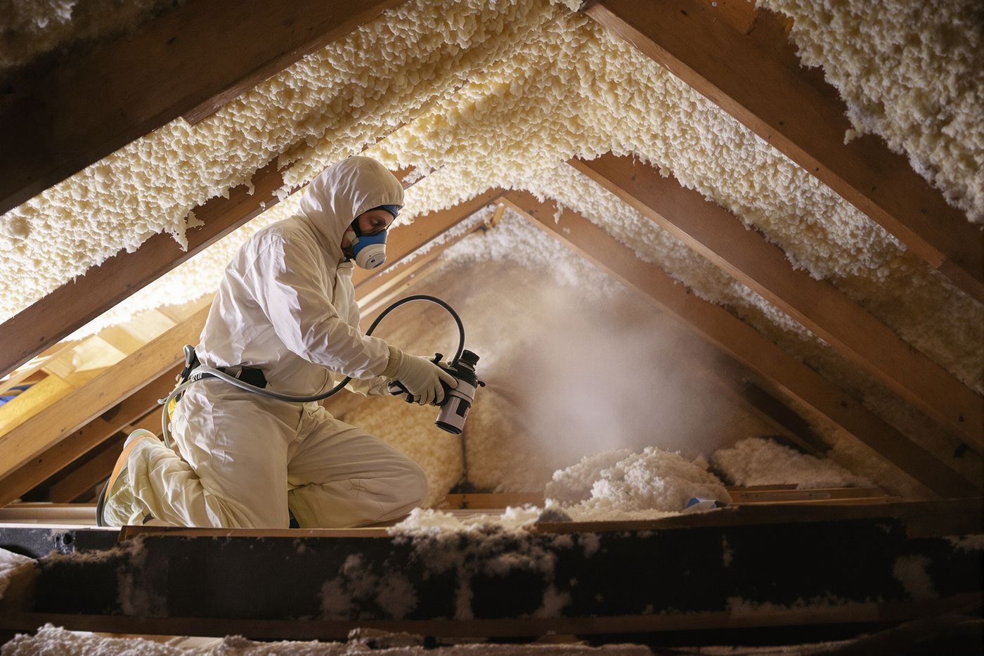 Installer applying spray foam insulation to the underside of an attic roof deck in a Tulsa home